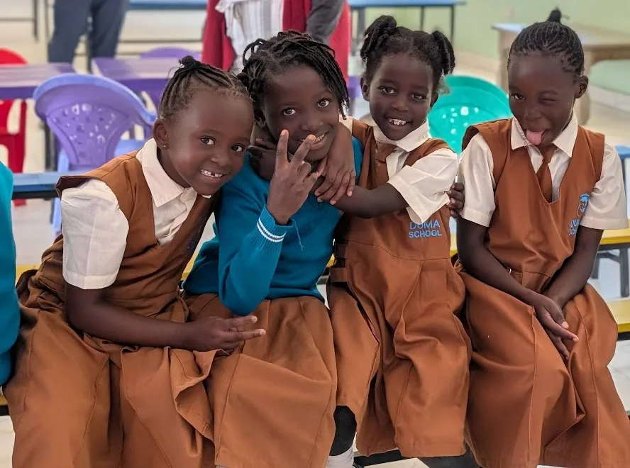 Four DUMA pupils smiling and sitting closely together in their classroom.